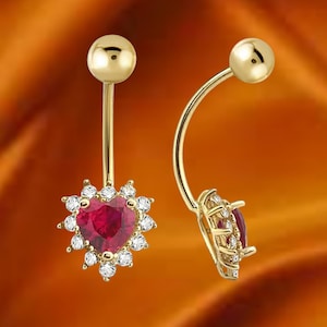 May include: Two gold-colored belly button rings. One ring features a heart-shaped, red gemstone surrounded by small, clear gemstones. The other ring has a similar design. The background is a gradient of orange and yellow.