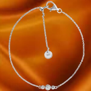May include: A delicate silver bracelet with three clear, round gemstones. The bracelet features a fine chain and an adjustable length with a small, round tag. The clasp is a lobster claw style.