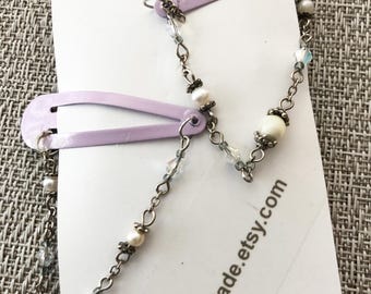 Könnte beinhalten: Zwei lila Haarspangen, verbunden durch eine dekorative Kette mit weißen Perlen und klaren Kristallen. Die Kette ist mit kleinen Metallschlaufen an den Spangen befestigt. Der Text "HahnMade.etsy.com" ist auf der weißen Karte zu sehen.