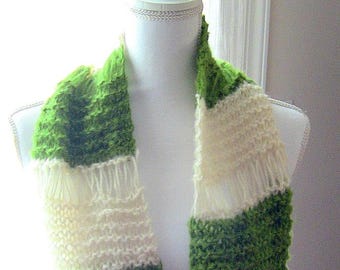 Könnte beinhalten: Handgestrickter Schal in Grün und Creme. Der Schal hat abwechselnde Streifen aus strukturiertem grünem und cremefarbenem Strick, mit Fransen an den Enden. Der Schal wird auf einer Schaufensterpuppe präsentiert.