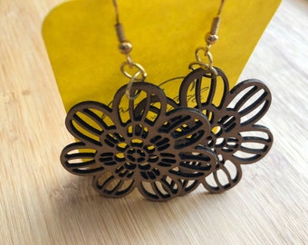 Könnte beinhalten: Ein Paar dunkelbraune Holzohrringe mit einem lasergeschnittenen Blumendesign und komplizierten Blütenblattausschnitten. Die Ohrringe sind an goldfarbenen Metallhaken befestigt und bilden einen hängenden Stil mit detailliertem Muster.