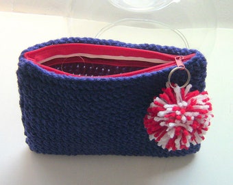 Könnte beinhalten: Ein marineblaues Häkel-Etui mit rotem Innenfutter und einem rosa Reißverschluss. Ein rot-weiß-blauer Pompon ist am Reißverschlussanhänger befestigt. Das Etui ist geöffnet und zeigt das rote Innenfutter.