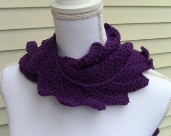 Könnte beinhalten: Ein tiefvioletter, gehäkelter Cowl-Schal mit einem gerüschten Rand. Der Schal wird auf einer weißen Schaufensterpuppe präsentiert, die die Textur und das Design des handgefertigten Accessoires hervorhebt. Der Cowl hat eine satte, einfarbige Farbe, perfekt für Wärme und Stil.