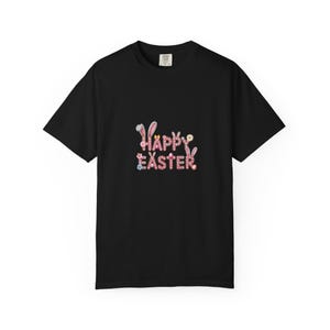 Peut inclure: T-shirt noir avec l'inscription "HAPPY EASTER" dans une police fantaisiste. Les lettres sont décorées d'oreilles de lapin, de fleurs et de couleurs pastel, parfait pour les célébrations de Pâques.