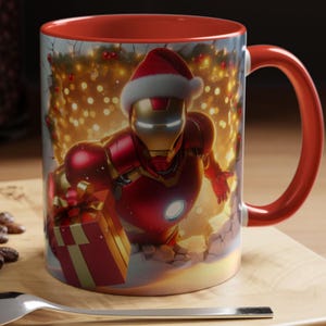 Peut inclure: Mug en c&eacute;ramique rouge et dor&eacute;e repr&eacute;sentant Iron Man avec un chapeau de P&egrave;re No&euml;l, tenant un cadeau emball&eacute;. L'int&eacute;rieur et la poign&eacute;e sont rouges. Le fond montre des lumi&egrave;res de No&euml;l et une sc&egrave;ne enneig&eacute;e.