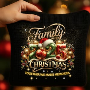 Peut inclure: Coussin en tricot noir avec l'inscription dorée "Family Christmas 2025" et des décorations festives. Le motif comprend un bonnet de Père Noël, des boules de Noël et la phrase "Together we make memories".