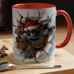 Peut inclure: Mug en c&eacute;ramique avec int&eacute;rieur et anse rouges, repr&eacute;sentant Batman avec un bonnet de P&egrave;re No&euml;l per&ccedil;ant un mur. Le design comprend un cadeau de No&euml;l et des lumi&egrave;res festives.