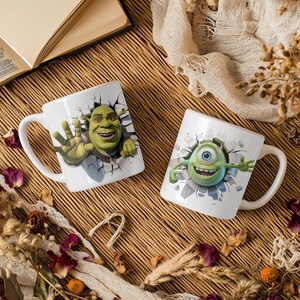 May include: Two white ceramic mugs with cartoon character designs. One mug features Shrek, the other features Mike Wazowski from Monsters, Inc. Both designs appear to be breaking through a wall. The mugs have white handles.
