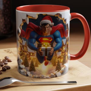Peut inclure: Mug en c&eacute;ramique avec int&eacute;rieur et anse rouges. L'ext&eacute;rieur pr&eacute;sente un motif festif de Superman portant un bonnet de P&egrave;re No&euml;l, tenant un coffret cadeau, avec une sc&egrave;ne de village de No&euml;l. Le mug est pos&eacute; sur une surface en bois.