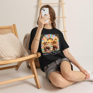 Peut inclure: Un t-shirt noir avec un motif coloré représentant deux petits chiens à motifs floraux, un soleil éclatant et une croix blanche. Le texte "His Mercies are New Every Morning" et "Lamentations 3:22-23" est écrit en dessous en police cursive.