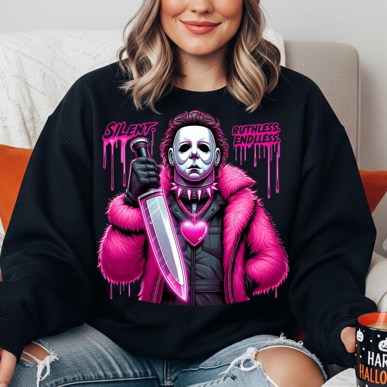 May include: Black sweatshirt featuring a graphic of a masked figure in a pink fur coat, holding a large knife. The design includes the words "SILENT" and "RUTHLESS: ENDLESS" in pink dripping font. A heart-shaped pendant is visible.