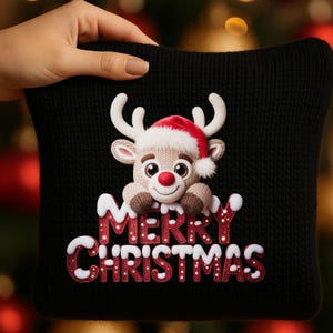 Peut inclure: Coussin de Noël en tricot noir avec un renne portant un bonnet de Père Noël. Le renne a un nez rouge et sourit. Les mots "MERRY CHRISTMAS" sont écrits en blanc et rouge.