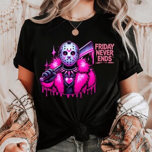 May include: Black t-shirt featuring a graphic of a hockey mask-wearing figure holding a cleaver, with a pink fur collar and the text "FRIDAY NEVER ENDS." The design includes pink accents and dripping effects, creating a bold, eye-catching look.