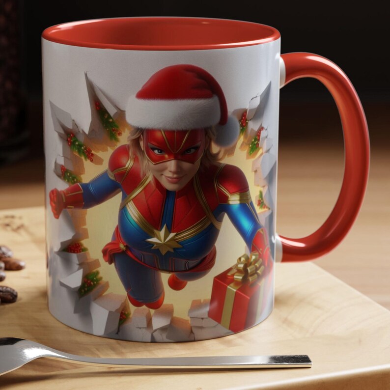 Peut inclure: Mug en c&eacute;ramique blanche avec int&eacute;rieur et anse rouges. La tasse pr&eacute;sente une super-h&eacute;ro&iuml;ne portant un bonnet de P&egrave;re No&euml;l, brisant un mur avec des d&eacute;corations de No&euml;l. La super-h&eacute;ro&iuml;ne porte un costume rouge, bleu et or et tient un cadeau emball&eacute;.