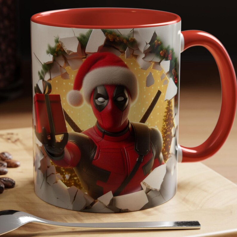 Peut inclure: Une tasse en c&eacute;ramique avec un int&eacute;rieur et une anse rouges. La tasse pr&eacute;sente un graphisme de Deadpool portant un bonnet de P&egrave;re No&euml;l et tenant un cadeau, sur fond de mur en train de se briser. La tasse est pos&eacute;e sur une surface en bois.