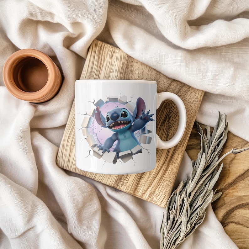 May include: White ceramic mug featuring a cartoon character, Stitch, breaking through a wall. The character is blue with large ears and a friendly expression. The mug has a white handle and is on a wooden surface.