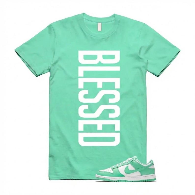 Pu&ograve; includere: Una maglietta verde menta con la parola "BLESSED" stampata verticalmente in bianco. Un paio di scarpe da ginnastica verde menta e bianche sono in primo piano, a complemento della combinazione di colori della maglietta. Le scarpe da ginnastica hanno un logo bianco.