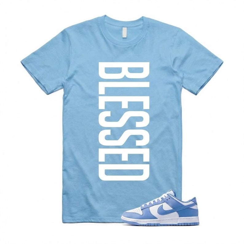 Pu&ograve; includere: Una maglietta azzurra con la parola "BLESSED" stampata verticalmente in bianco. Un paio di scarpe da ginnastica azzurre e bianche sono posizionate davanti alla maglietta.