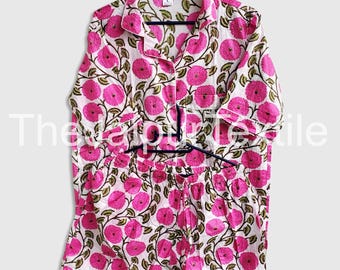 May include: A two-piece pajama set with a white background and a repeating pattern of large pink flowers and green leaves. The set includes a button-down shirt and shorts, both hanging on a black hanger. The text "The Jaipur Textile" is partially visible.