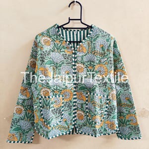 May include: A quilted jacket with a floral pattern in shades of green, yellow, and blue. The jacket has a striped trim and is hanging on a black hanger. The text "The Jaipur Textile" is visible on the front.