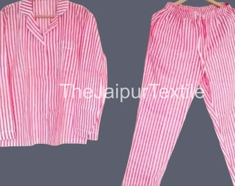 May include: A pink and white striped pajama set. The set includes a button-down shirt with a chest pocket and matching pants with a drawstring waist. The pajamas are hanging on wooden hangers against a gray background.
