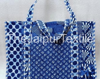 May include: A blue tote bag with various patterns, including polka dots, spirals, and leaf-like designs. The bag has two handles and is made of quilted fabric. The text "the jaipur textile" is visible on the bag.