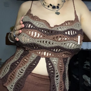 May include: A brown, beige, and gray crochet top with a scalloped neckline and spaghetti straps. The open-weave design features horizontal stripes of varying shades. This handmade top is a unique piece of apparel.