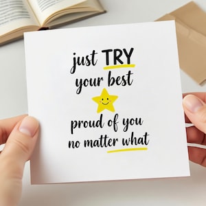 May include: A white greeting card with black script that reads "just TRY your best" and "proud of you no matter what." A yellow star with a smiling face is in the center. The card is held by two hands.