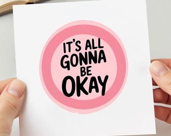Könnte beinhalten: Eine weiße quadratische Karte mit dem Text "IT'S ALL GONNA BE OKAY" in Schwarz, innerhalb eines rosa Kreises mit einem rosa Rand. Die Karte wird von zwei Händen gehalten.