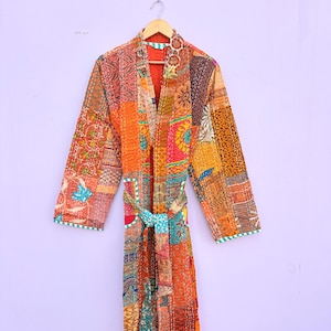 Pode incluir: Robe de patchwork em tons de laranja, vermelho e castanho, com cinto a condizer. O robe é feito de vários padrões e texturas de tecido. As mangas e as bordas são aparadas com uma borda branca e verde.