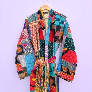 May include: A patchwork robe with a vibrant mix of colors and patterns. The robe features a tie belt and long sleeves. The design incorporates various fabrics and textures, creating a unique and artistic look. The robe is hanging on a wooden hanger.