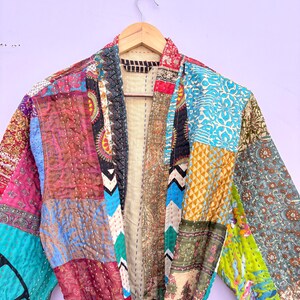 May include: A patchwork robe with a variety of colorful fabric patterns. The robe is hanging on a wooden hanger. The fabrics include floral, geometric, and paisley designs in shades of blue, red, green, and pink.