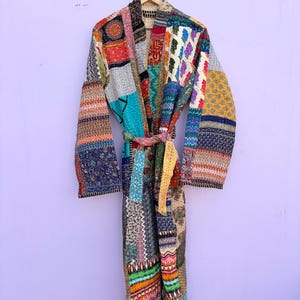 May include: A patchwork robe with a variety of colorful fabric patterns. The robe is hanging on a wooden hanger. The robe has a belt made of the same patchwork fabric. The robe is approximately 55 inches long.