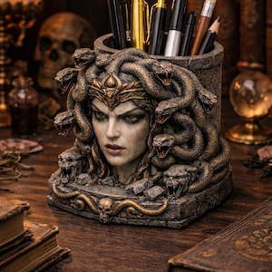 Op de afbeelding: Een gedetailleerde pennenhouder met een gebeeldhouwde Medusa-kop met slangen als haar. De houder is gemaakt van een steenachtig materiaal met gouden accenten en is gevuld met pennen en potloden. Het ontwerp is ingewikkeld en gotisch.