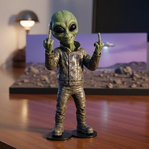 Può includere: Una statuetta di alieno verde, che mostra il dito medio con entrambe le mani. La figura indossa una giacca e pantaloni metallici. Un piccolo diorama di un paesaggio desertico con un UFO è sullo sfondo.