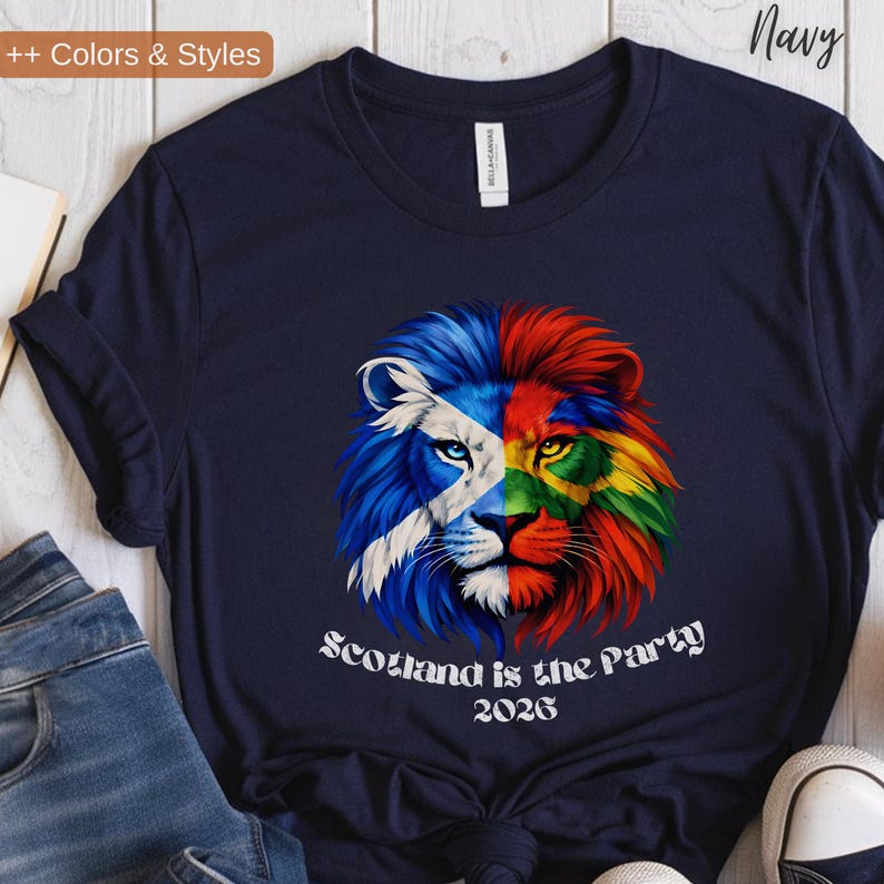 May include: Navy blue t-shirt featuring a colorful lion design. The lion's face is split, with one side displaying the Scottish flag and the other side a vibrant rainbow of colors. The text "Scotland is the Party 2026" is printed below the lion.