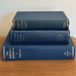 May include: Three hardcover books stacked on a wooden surface. The books are dark blue with gold lettering. Titles include "The Writer's Handbook," "The Oxford Book of American Verse," and "Words and Their Uses."