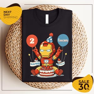 A black t-shirt with a graphic design of a cartoon character wearing a party hat and holding a birthday cake, with balloons and the text "Lucas" and "Happy Birthday" printed on it.