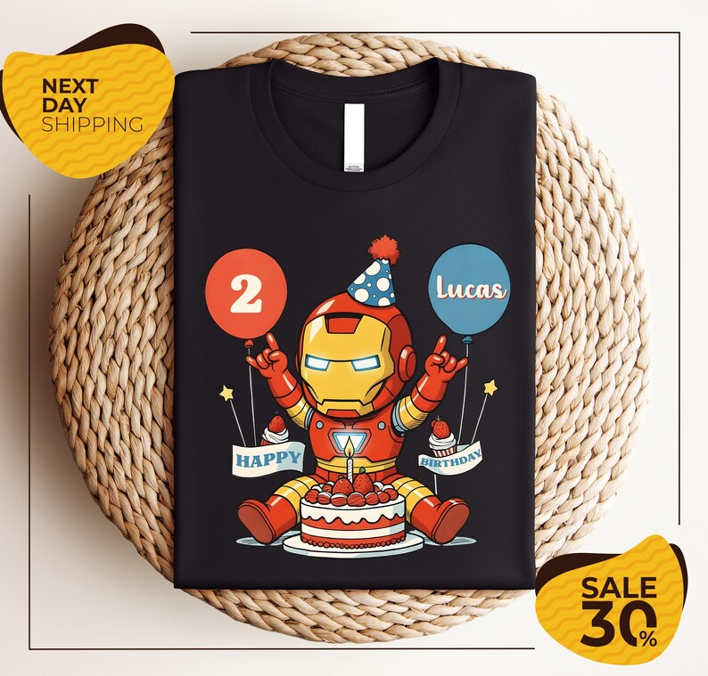 A black t-shirt with a graphic design of a cartoon character wearing a party hat and holding a birthday cake, with balloons and the text "Lucas" and "Happy Birthday" printed on it.