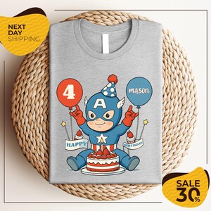 A gray t-shirt with a cartoon image of a superhero character wearing a party hat and holding balloons, celebrating a birthday.