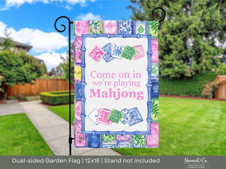 May include: A double-sided garden flag with a watercolor design. The flag features the text "Come on in we're playing Mahjong" in pink. The flag is 12x18 inches and has a bamboo-style border with pink, blue, and green accents. The background shows a residential yard.