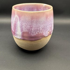 Könnte beinhalten: Eine handgefertigte Keramikschale mit runder Form. Der obere Teil ist hellviolett mit einer strukturierten, weißen Glasur, während die untere Hälfte eine natürliche, unglasierte, beige Farbe hat. Die Schale eignet sich zum Servieren von Speisen.