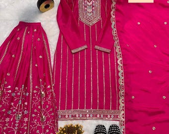 Può includere: Un vivace completo indiano fucsia. Il set include una tunica a maniche lunghe con ricami argentati, una gonna abbinata e una sciarpa. L'outfit è completato da scarpe bianche e nere decorate.