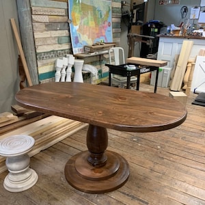 May include: A dark brown oval wooden table with a pedestal base. The table top is smooth and has a slight sheen. The base is turned wood with a fluted design. The table is sitting on a wooden floor.