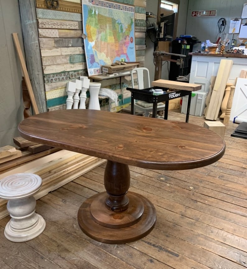 May include: A dark brown oval wooden table with a pedestal base. The table top is smooth and has a slight sheen. The base is turned wood with a fluted design. The table is sitting on a wooden floor.