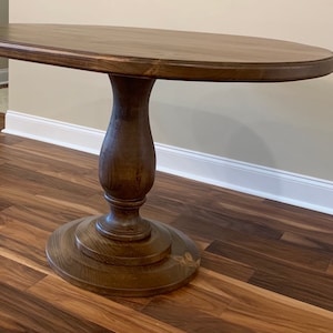 May include: A dark brown oval wooden table with a pedestal base. The table has a smooth, polished finish and a simple, elegant design.