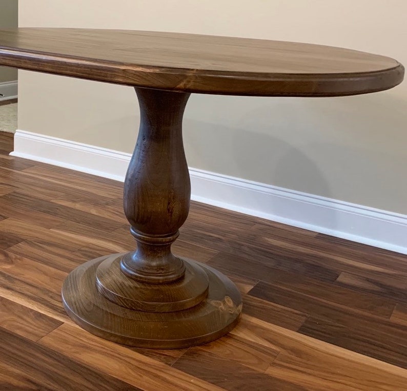 May include: A dark brown oval wooden table with a pedestal base. The table has a smooth, polished finish and a simple, elegant design.
