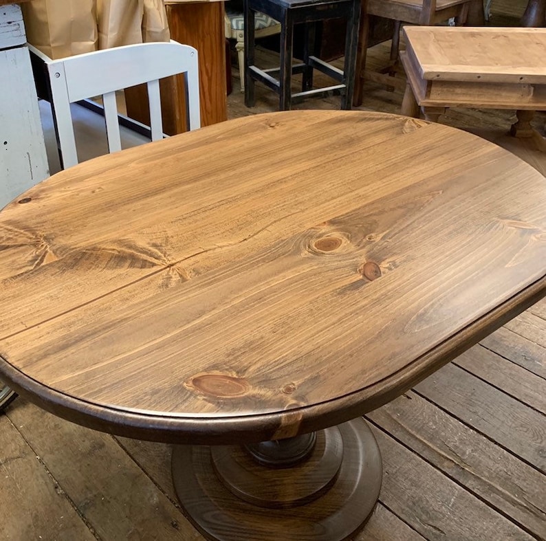 May include: A round wooden table with a pedestal base. The table top is a rich brown colour and has a natural wood grain finish. The base is also brown and has a slightly darker finish.