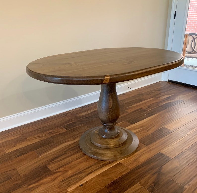 May include: A dark brown oval wooden table with a pedestal base. The table is on a hardwood floor.