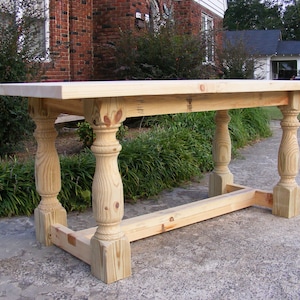 May include: A wooden table with a natural finish and turned legs. The table has a rectangular top and a simple design.